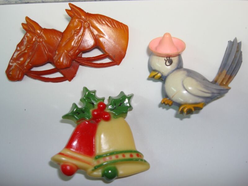 Vintage celluloid pins from the 1930s-40s, including a Hallmark Christmas pin, a horse heads pin, and a Bluebird of Happiness pin.