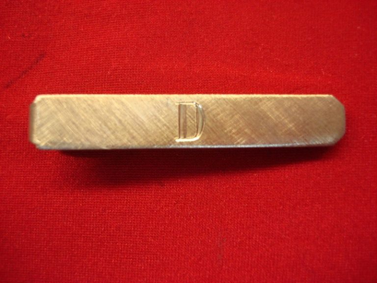 Vintage gold-tone tie clip with engraved 'D', unique matte finish