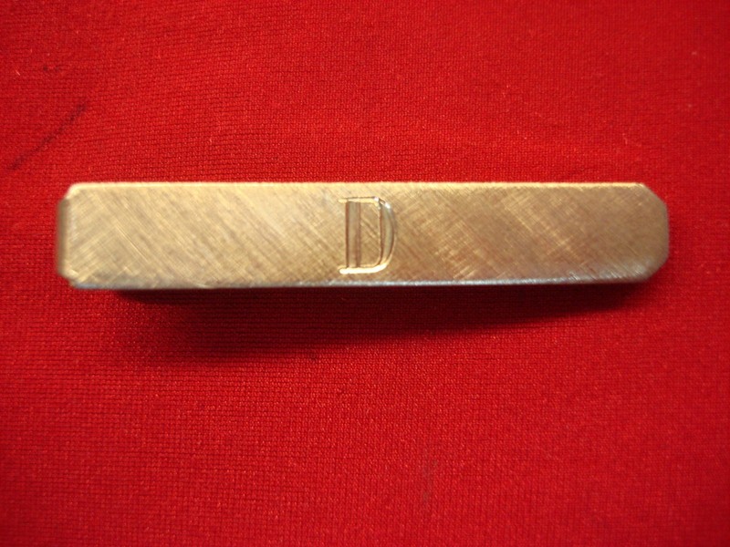 Vintage gold-tone tie clip with engraved 'D', unique matte finish