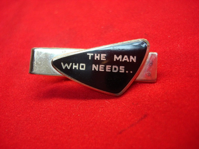 Vintage gold-tone tie clip with black enamel inscription 'The Man Who Needs...'