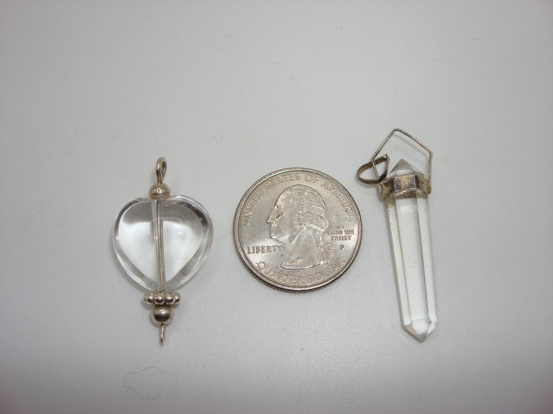 Two silver rock crystal quartz pendulums, one heart-shaped and one larger oval.