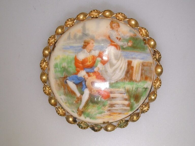 Antique porcelain pin with gold-washed frame, depicting a scene of a young couple by a stream.
